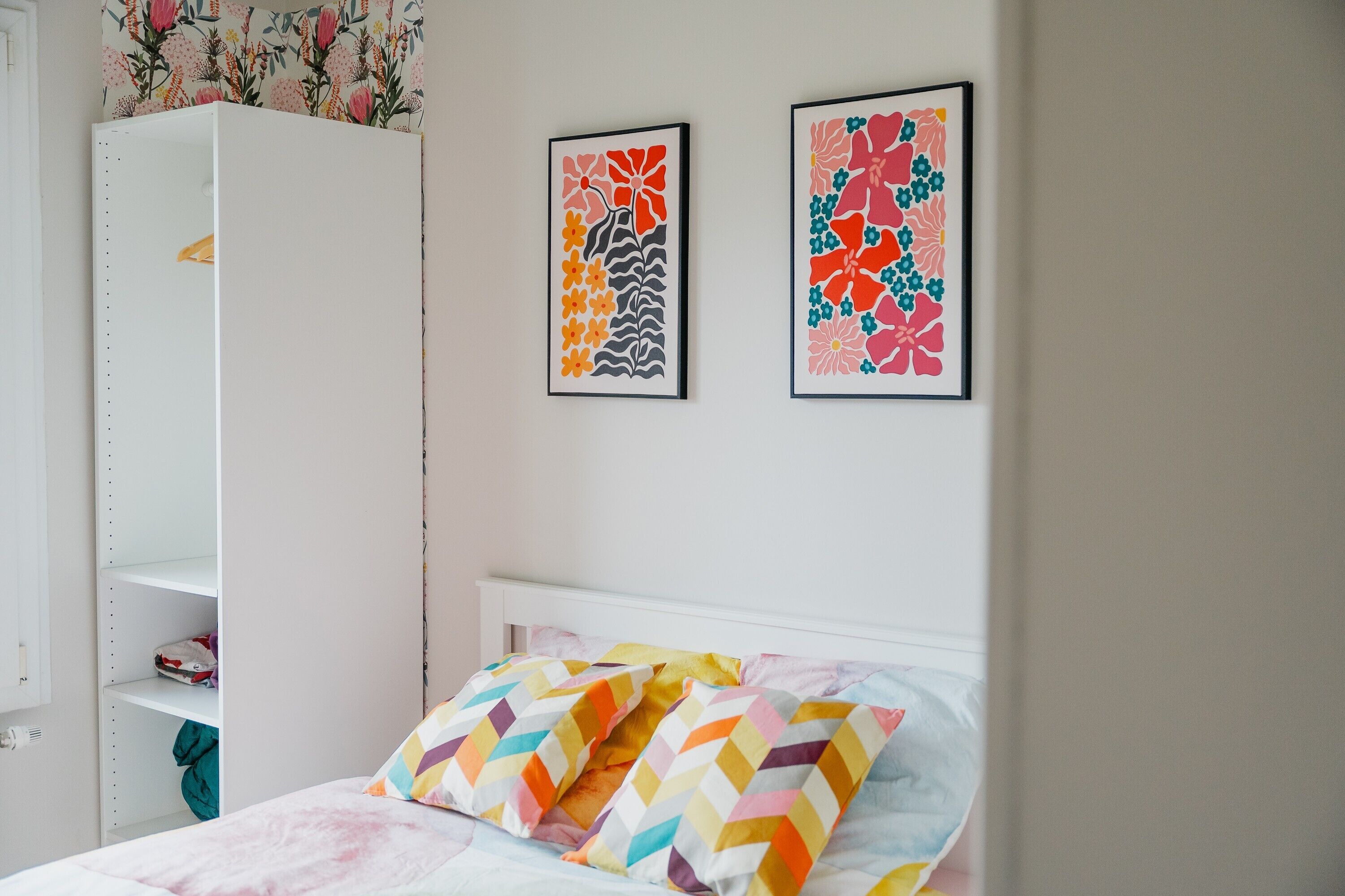 A bedroom with a bed, a wardrobe, and two framed floral artworks on the wall.