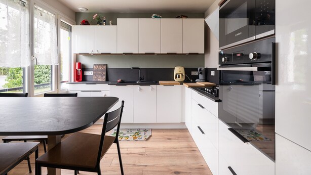 Une cuisine moderne avec des meubles blancs, un four Bosch et un coin repas comprenant une table et des chaises.
