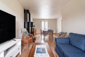 A living room with a TV, sofa, dining table, chairs, and a fireplace. - Holiday Home 'De L'enclume' with Private Garden, Balcony and Wi-Fi (Sévignac)