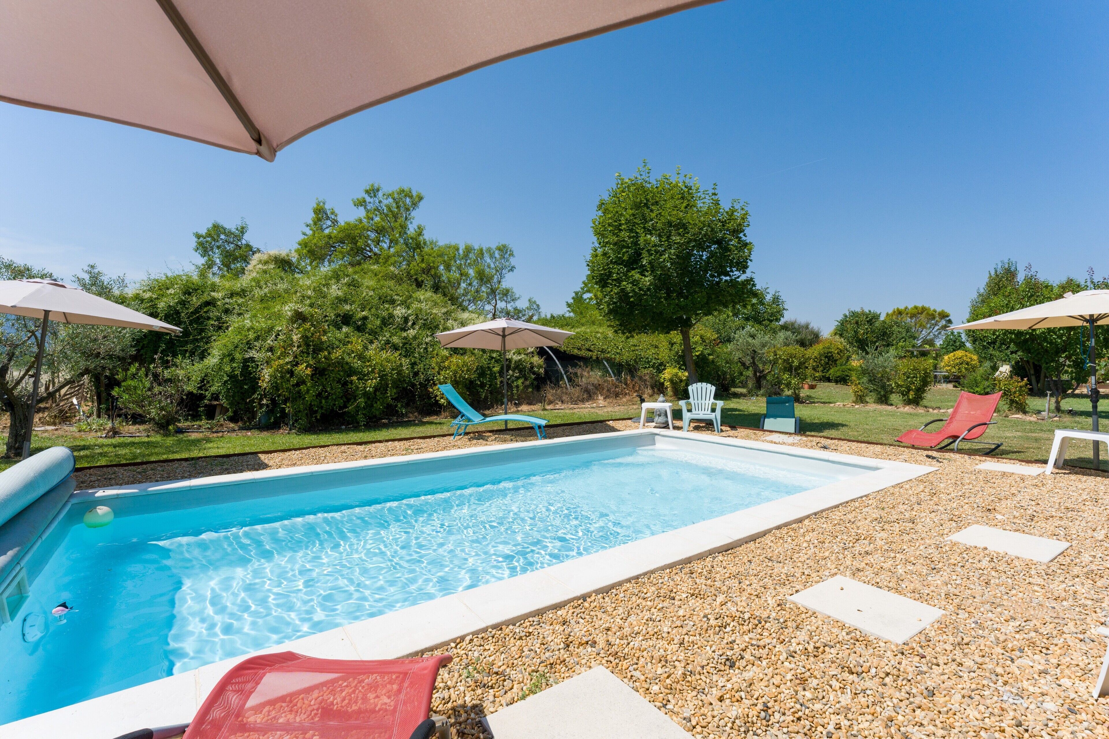 A rectangular swimming pool with a pebble deck, surrounded by lounge chairs and umbrellas.