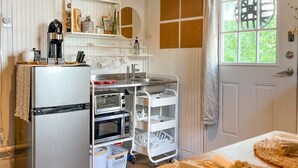 A kitchen with a refrigerator, microwave, and oven. There is a white cart with baskets and a table with a woven placemat.