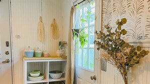 A kitchen with wooden cabinets, a window with curtains, and a table with a woven placemat and utensils.