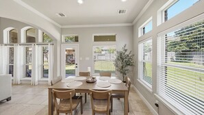 A dining area with a table set for four, a potted plant, and a view of the backyard through large windows. - Cozy, Quiet 4-bedroom, 3.5 bathroom Home in The Woodlands (Magnolia)