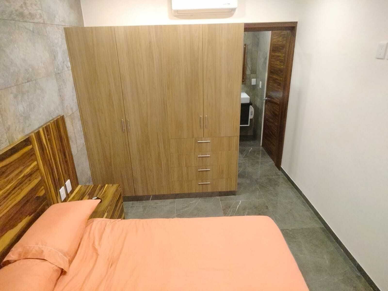 Une chambre à coucher avec un lit, une armoire et une salle de bain visible à travers une porte ouverte.