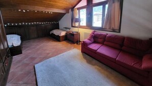A cozy attic bedroom with a wooden ceiling, a red sofa, a small bedside table, and a window with curtains. - 100m from ski slopes, 2nd floor, balcony, tv, ski locker, 58m², Montgenèvre (Montgenèvre)