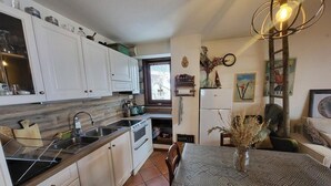 A compact kitchen with white cabinets, a sink, and a stove. There's a dining table with a patterned tablecloth and chairs. - 100m from ski slopes, 2nd floor, balcony, tv, ski locker, 58m², Montgenèvre (Montgenèvre)