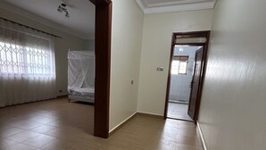 Una habitació àmplia amb terres de fusta, un gran finestral amb vistes i una porta que condueix a una altra habitació.