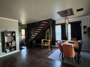 A spacious living area with a wooden staircase, a dining table with chairs, and a bookshelf. - Adults only Sanctuary & Writer's Retreat (Manchaca)