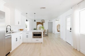 A modern kitchen with white cabinetry, a built-in microwave, and pendant lighting.