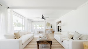 Un salon spacieux avec des canapés blancs, une table basse en bois et un ventilateur de plafond.