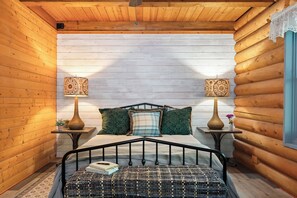 Um quarto de cabana rústica e acolhedor, com uma cama, duas mesas de cabeceira com abajures e uma janela com cortinas de renda.