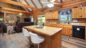 L’intérieur d’un chalet rustique, avec un plafond en bois, des murs en pierre, un coin cuisine et un espace salon doté d’une cheminée.