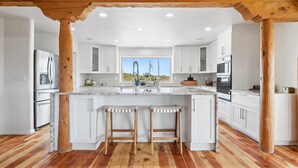 Una cucina moderna con mobili bianchi, una isola centrale con sgabelli, travi in legno e vista sul deserto.