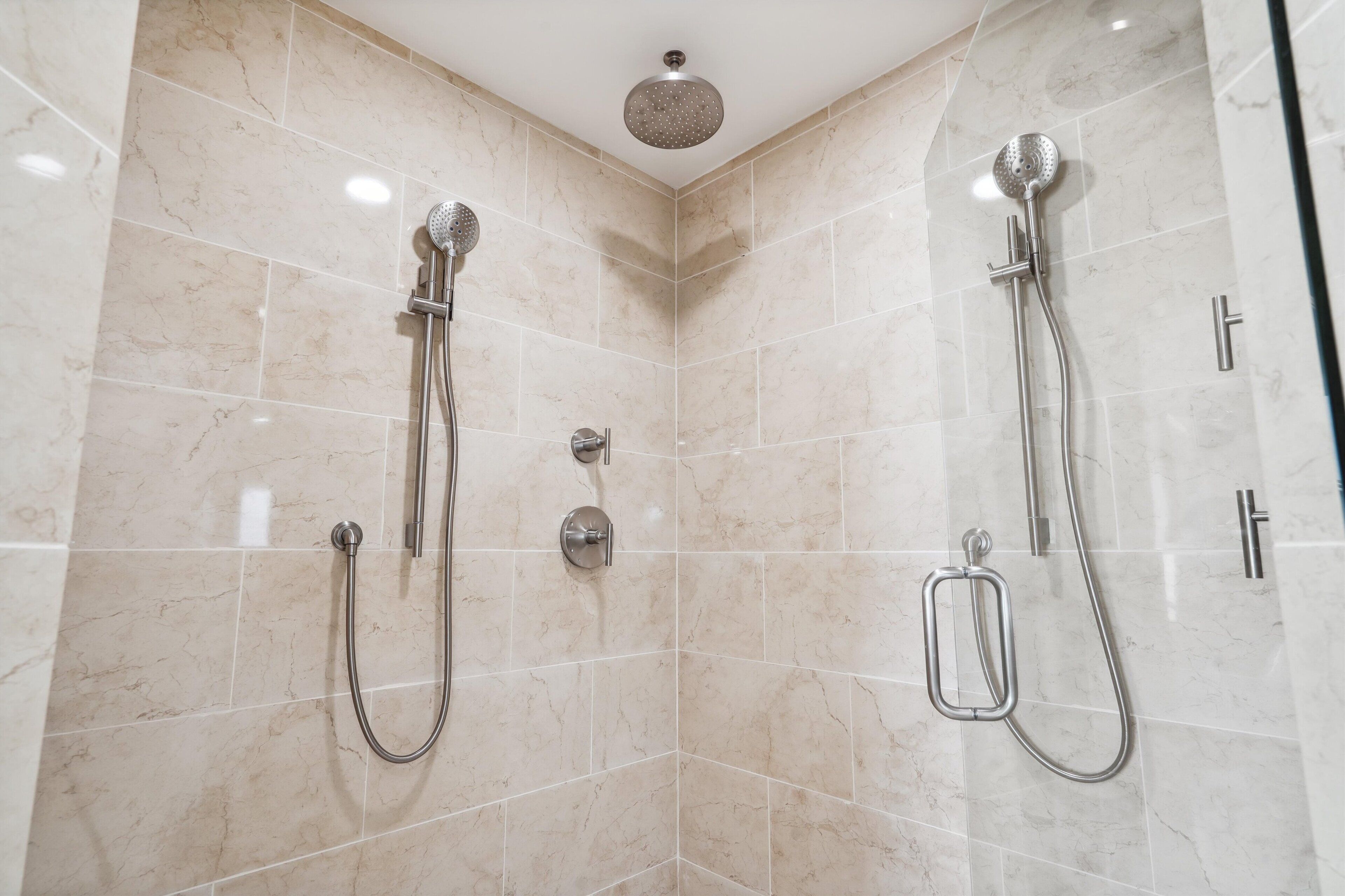 A modern shower area with two showerheads, a handheld shower, and a wall-mounted control panel.