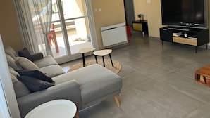 A modern living room with a grey sofa, a flat-screen TV, and a sliding glass door leading to an outdoor area. - Maison Avalone in the heart of the Ardèche Gorges! (Vallon-Pont-d'Arc)
