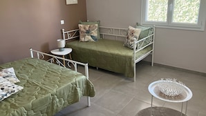 A bedroom with two beds, a small table with a lamp, and a window with a view of greenery. - Maison Avalone in the heart of the Ardèche Gorges! (Vallon-Pont-d'Arc)