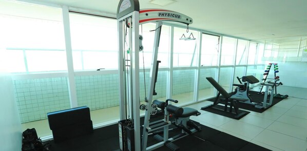 Un gimnasio con equipo de ejercicio diverso, ventanas amplias y piso de baldosas.