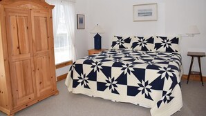 A bedroom with a bed, a wooden wardrobe, a nightstand, a lamp, and a framed picture on the wall. - Tori's Landing- Limited Water View Shared Pier Access (Chincoteague)