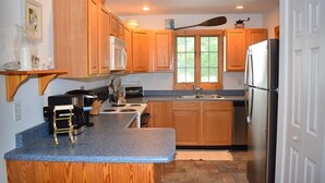 A kitchen with wooden cabinets, a stainless steel refrigerator, a microwave, and a stove. - Tori's Landing- Limited Water View Shared Pier Access (Chincoteague)