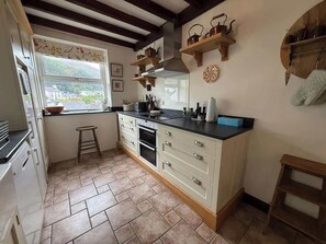 A kitchen with a window, wooden beams, a stove, and a sink.