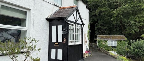 A traditional black and white building with a small black structure attached, a paved driveway, and potted plants.