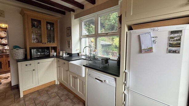 A kitchen with white cabinetry, a dishwasher, a refrigerator, and a window with a view of greenery.