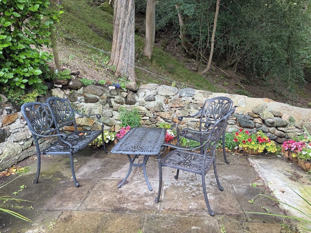 A patio with two metal chairs and a table, surrounded by a stone wall and potted plants.
