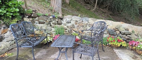 Un patio con dos sillas de metal y una mesa, rodeado por un muro de piedra y plantas en macetas.