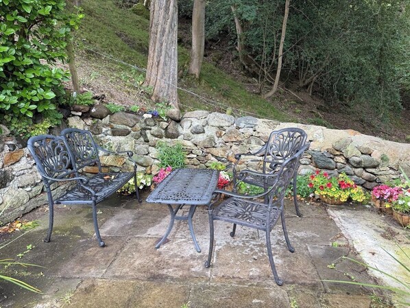 Un patio con dos sillas de metal y una mesa, rodeado por un muro de piedra y plantas en macetas.