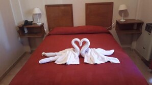 Ein Hotelzimmer mit rotem Bettbezug, zwei hölzernen Kopfteilen, Nachttischen mit Lampen und Handtüchern, die als Schwan auf dem Bett drapiert sind.