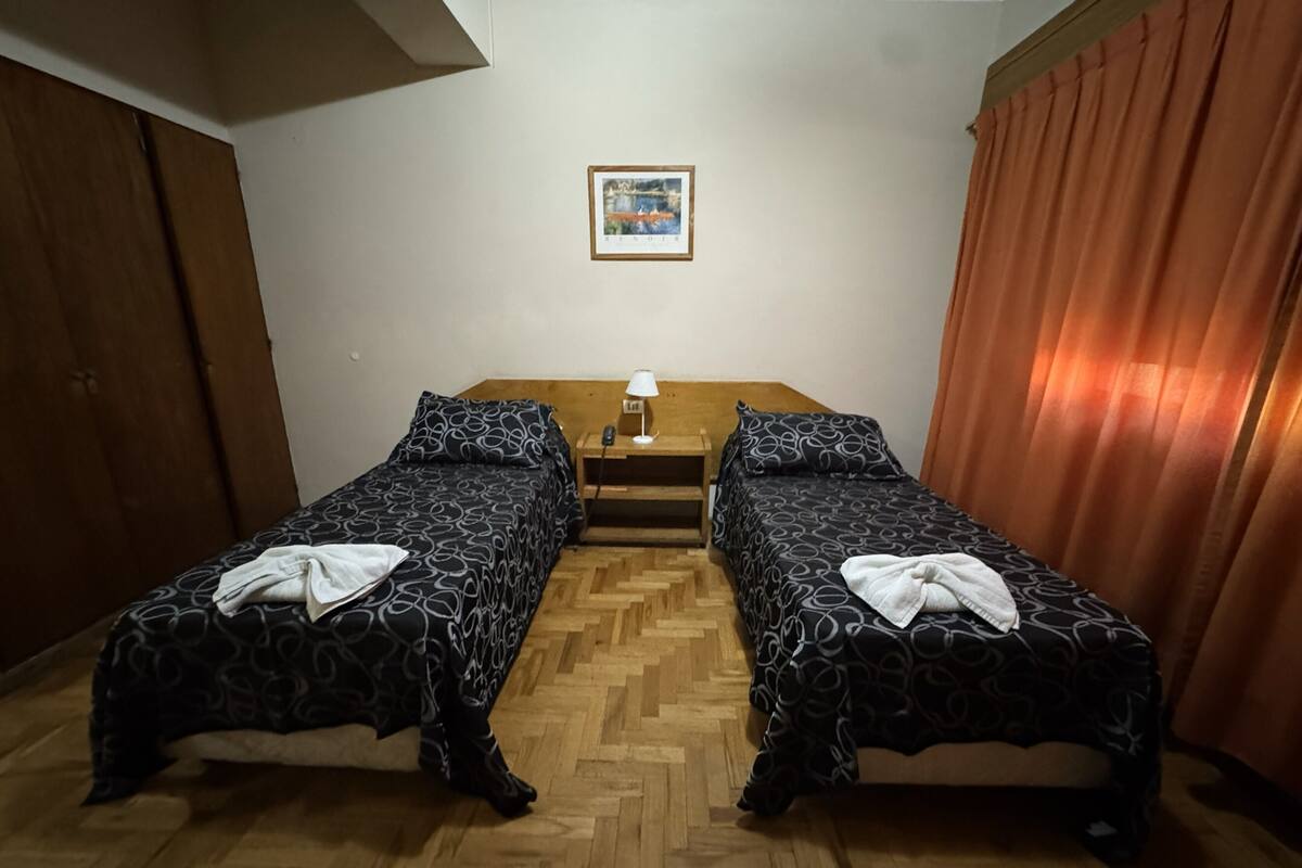A room with two beds, a wooden table, a lamp, and a painting on the wall.
