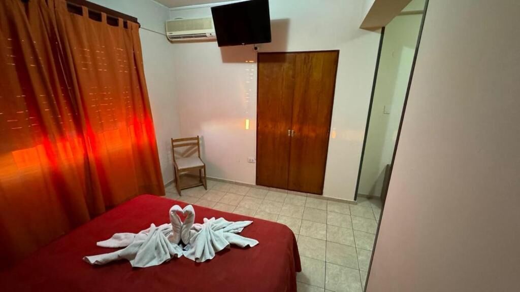 A hotel room with a bed, a wooden chair, a wardrobe, and a television mounted on the wall.