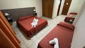 Ein Hotelzimmer mit zwei Betten, einem Holz-Kopfteil, einem Nachttisch mit Lampe sowie einem Badezimmer mit Dusche und Toilette.