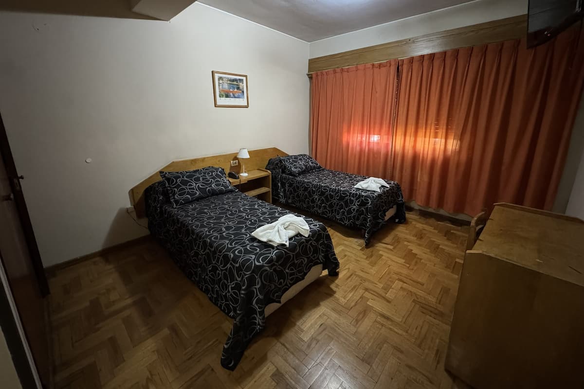 A hotel room with two beds, a nightstand, a lamp, a framed picture on the wall, and a wooden floor.