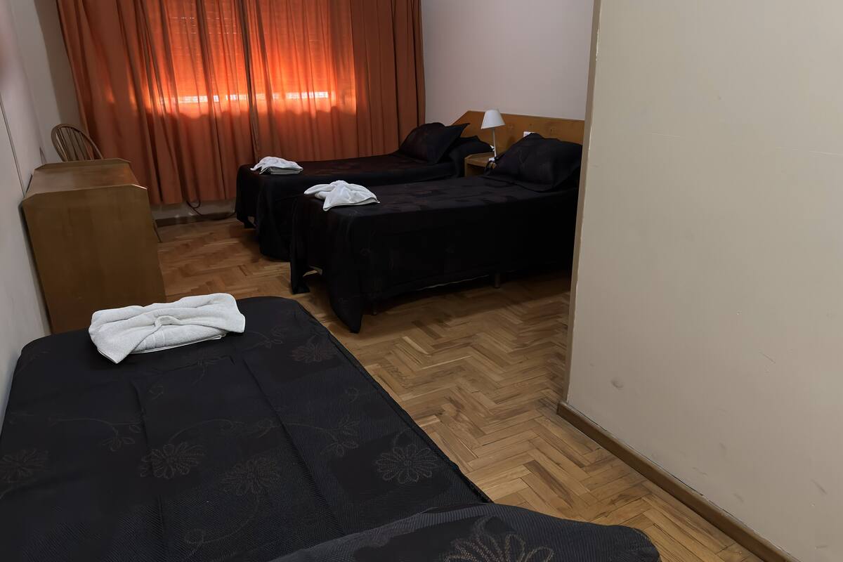 A hotel room with two beds, a wooden floor, a desk, and a chair.