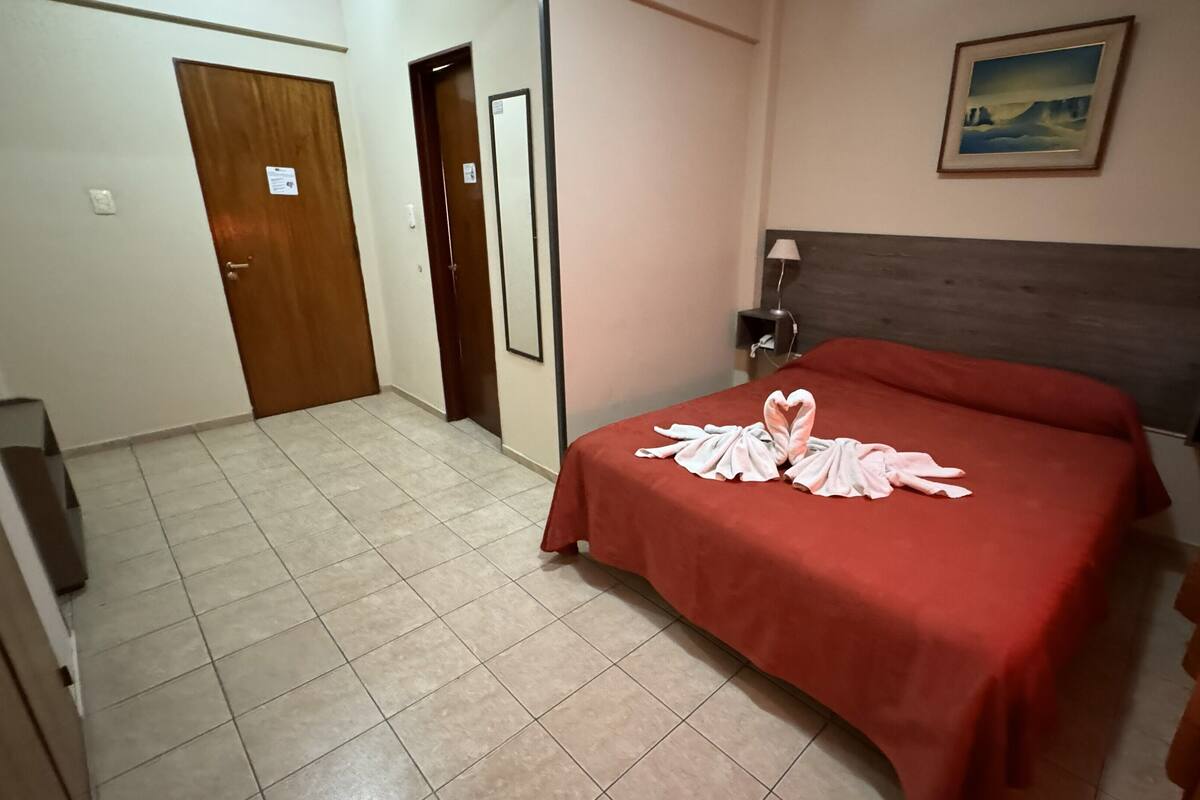 A hotel room with a bed, a painting on the wall, and a door.