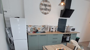 A modern kitchen with a dining area, featuring a refrigerator, microwave, sink, and a clock on the wall.