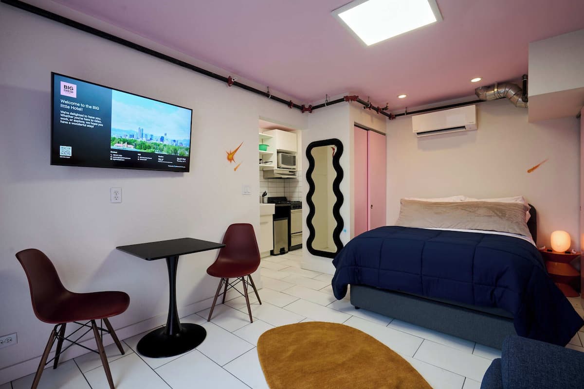 Habitación de hotel moderna con cama, escritorio, dos sillas, televisor y área de cocina.
