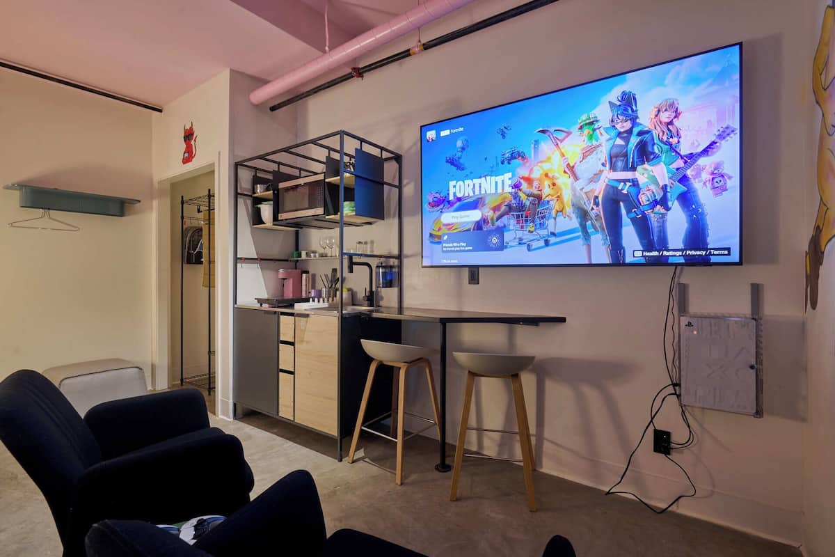 Habitación moderna con una pantalla grande mostrando un videojuego, una kitchenette y zona de estar.