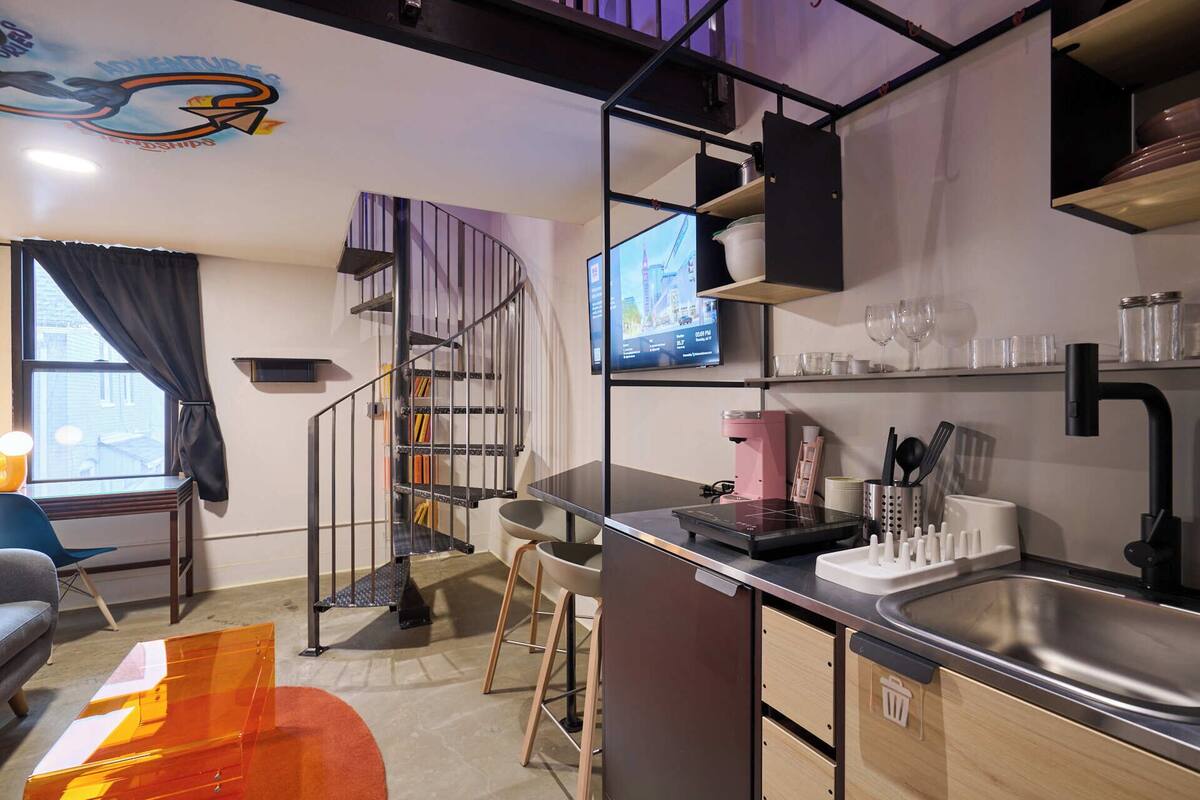 Una cocina moderna con un lavamanos de acero inoxidable, una cafetera y un televisor montado en la pared.