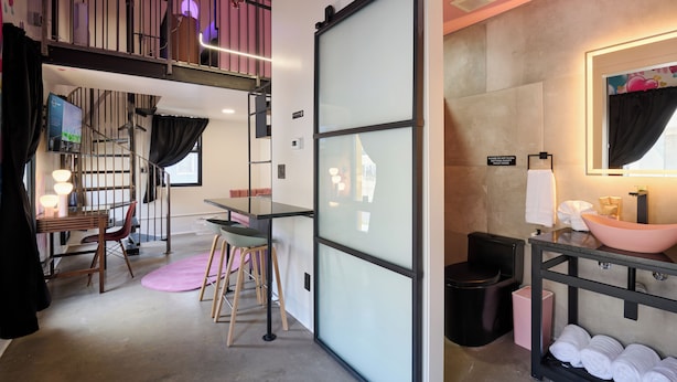 A compact hotel room with a loft bed, a small dining area, a bathroom with a large mirror and a pink sink. - BIG LITTLE HOTEL  (Denver)
