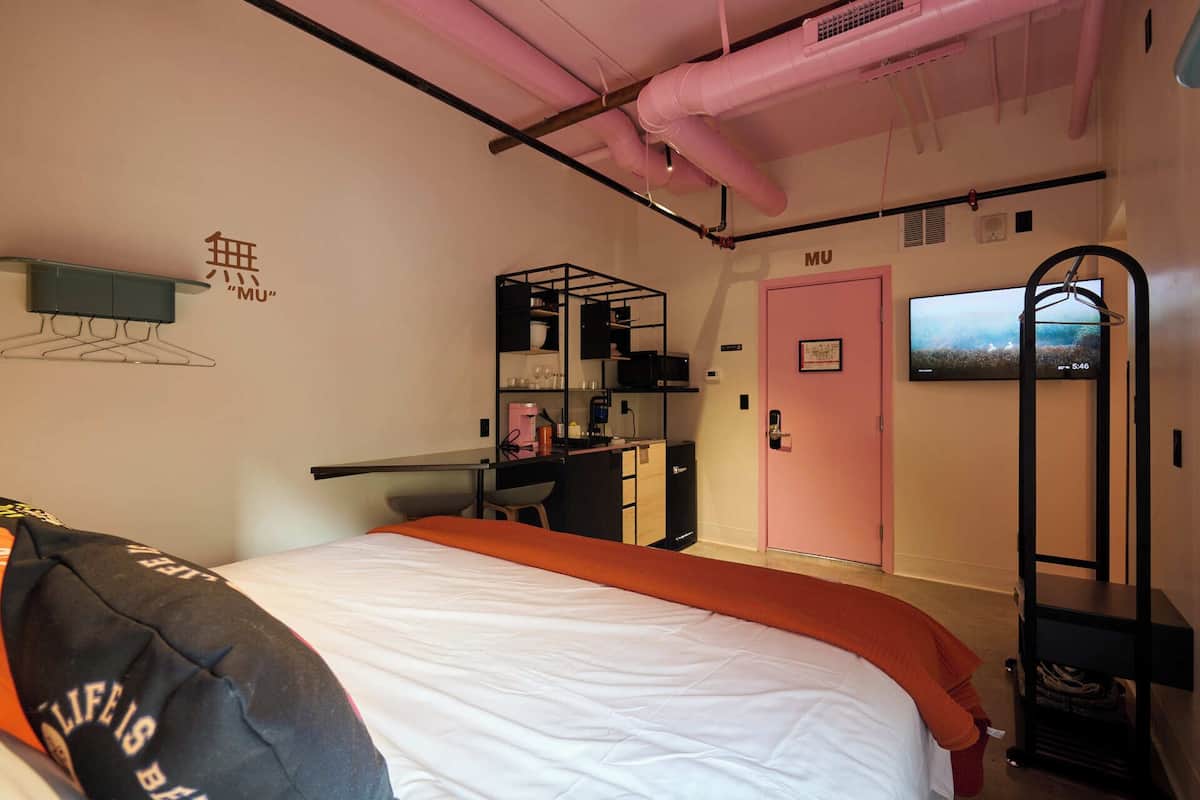 Un dormitorio pequeño con cama, una puerta rosa, televisión y una kitchenette.