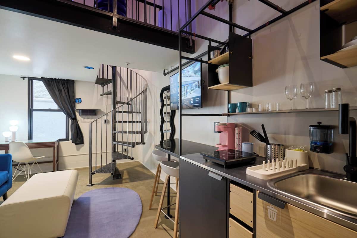 Una cocina compacta con lavavajillas integrado, cafetera y lavabo. Se ve una escalera que sube a un nivel superior.