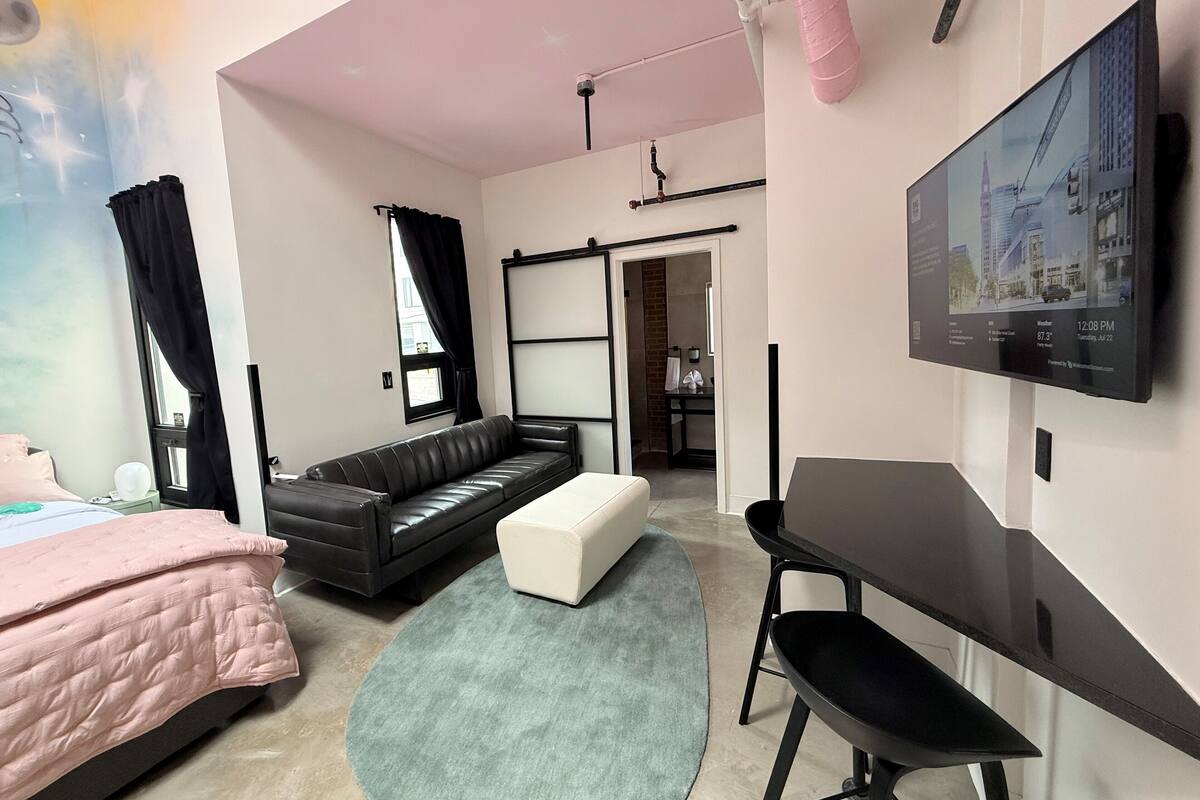 Una habitación de hotel moderna con cama, sofá, escritorio y televisor montado en la pared.