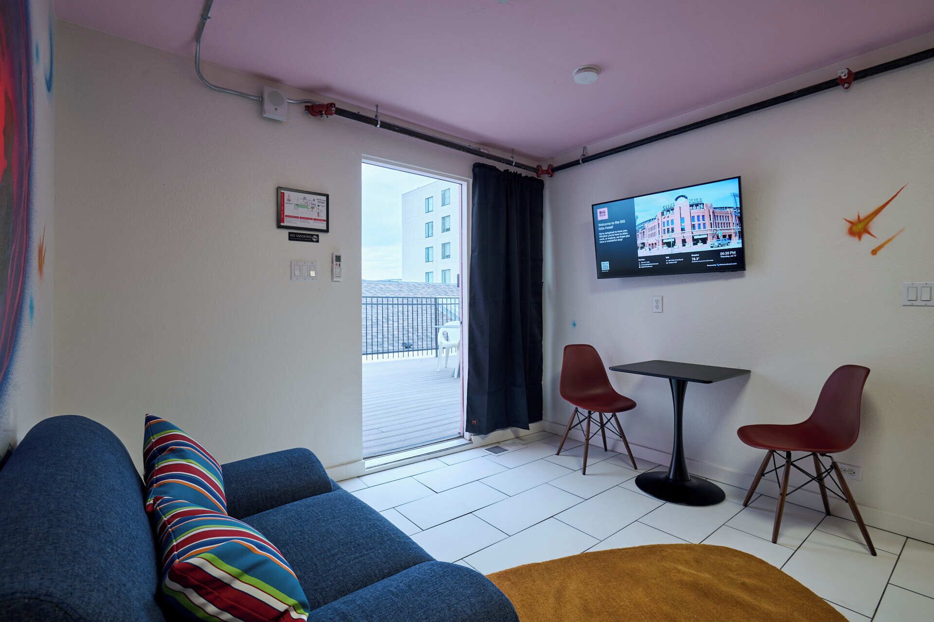 A modern living room with a sofa, two red chairs, a small table, and a TV mounted on the wall.