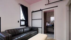 A modern living room with a black leather sofa, a white ottoman, and a sliding barn door leading to a bathroom. - BIG LITTLE HOTEL  (Denver)