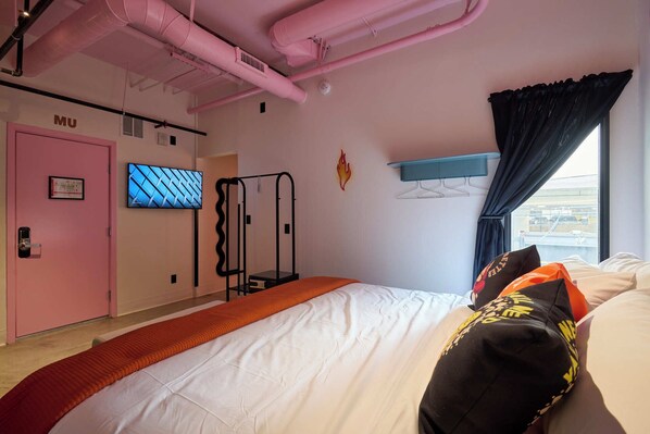 A bedroom with a bed, a pink door, a TV, a fire decal, and a window with curtains. - BIG LITTLE HOTEL  (Denver)