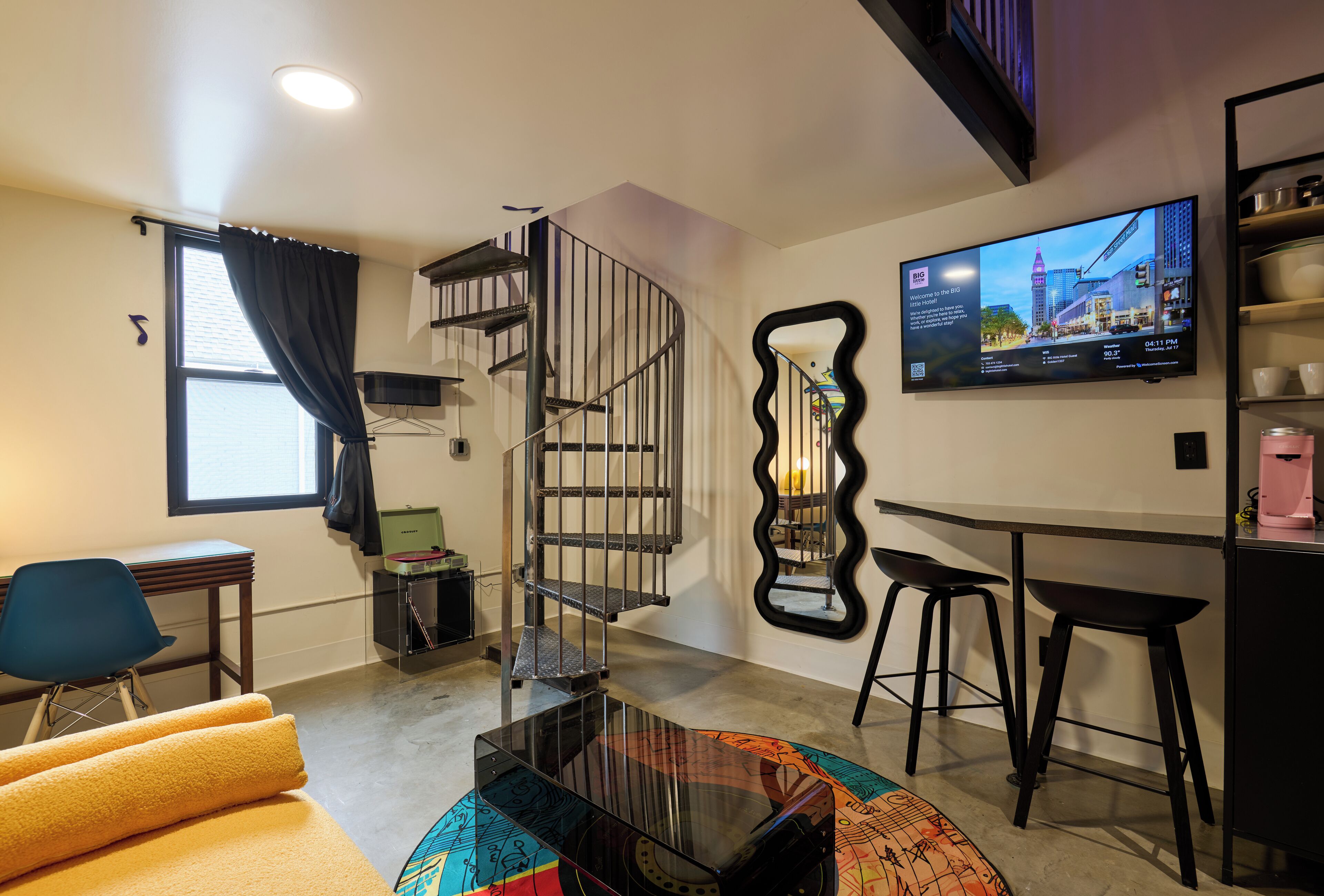 A modern living room with a spiral staircase, a flat-screen TV, and a coffee machine.
