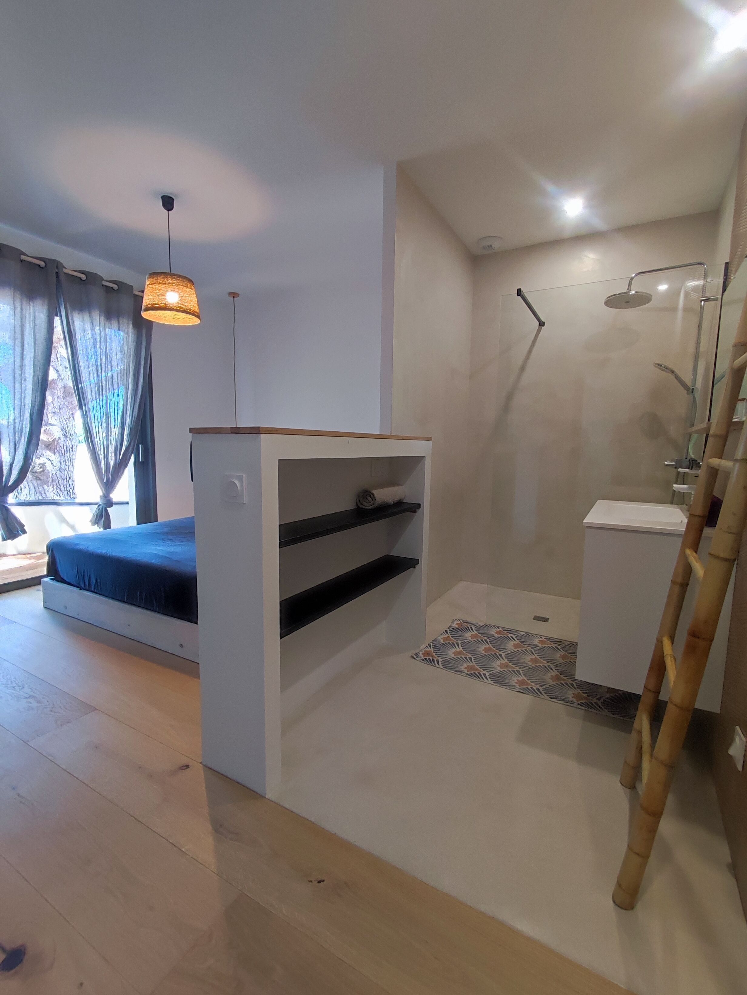 Quarto moderno com cama, um pequeno armário branco, área de chuveiro e escada de madeira.