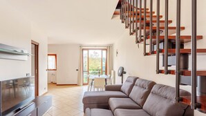 A modern living room with a sectional sofa, a flat-screen TV, and a staircase with wooden railings. - Cadrezzate With Osmate (VA) (Osmate)